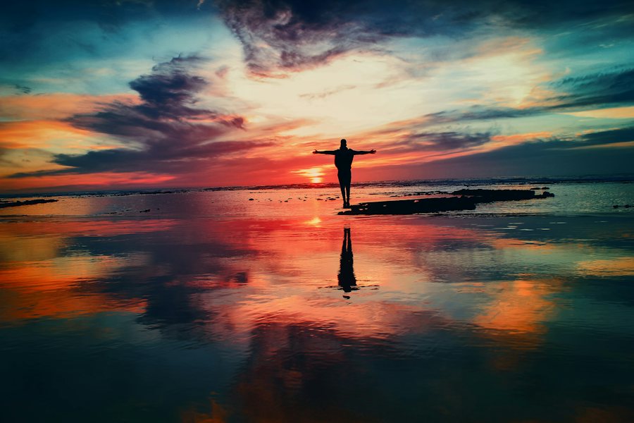 Person with open arms at sunrise by the water